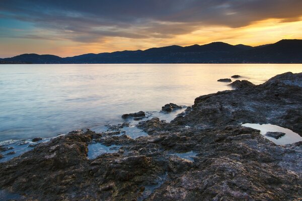 The grey rocky shore is washed by water