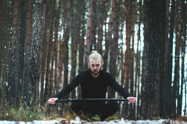 A man with a sword against the background of tree trunks