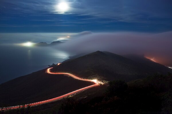 Longa estrada iluminada através das montanhas e do mar