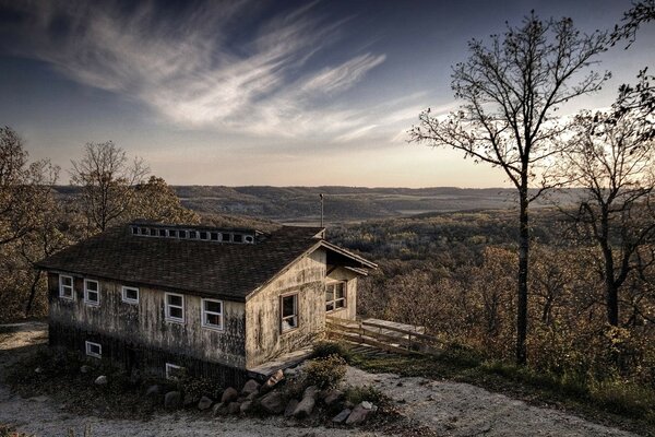 A picture of an abandoned house on a cliff rocks a lot of trees