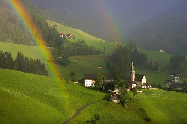 Beautiful summer lawn with a rainbow on the background of houses