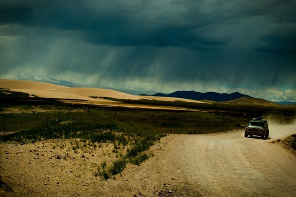 The car is driving along the road, and behind it is a darkness of dust