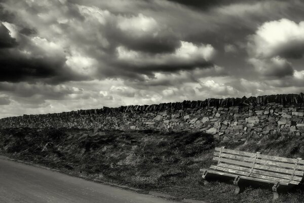 Schwarz-Weiß-Landschaft Bank und Autobahn im Vordergrund hinten viele Steine oben am Himmel mit Wolken