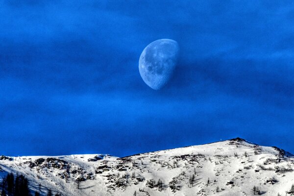 Mond auf dem Hintergrund der schneebedeckten Berge