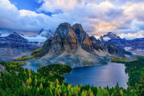 A blue lake surrounded by forests and mountains under a cloudy sky