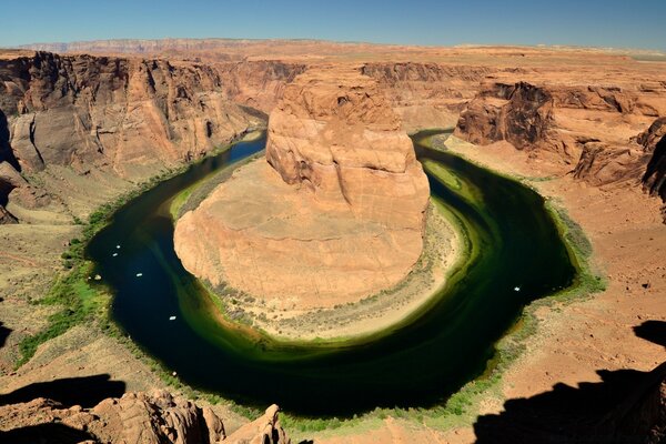 The greenish water of the river flows around a round fragment of the canyon