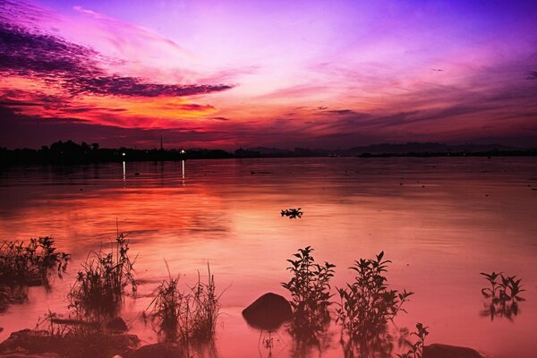 Sonnenuntergang auf einem breiten Fluss. Bunte gefiederte Wolken am Himmel