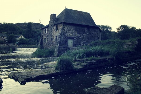 A gray house on the shore of a gloomy pond