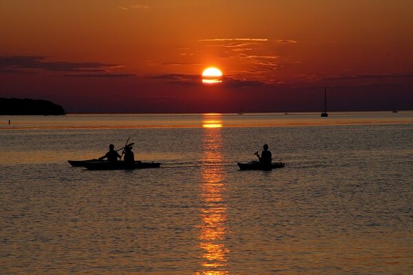 Persone in barche contro il sole al tramonto