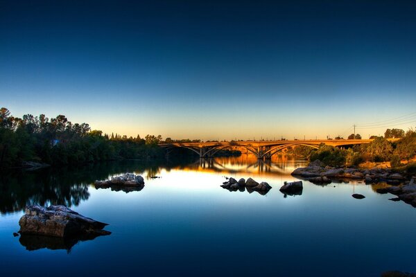 Un fiume con un cielo blu riflettente e un ponte in lontananza