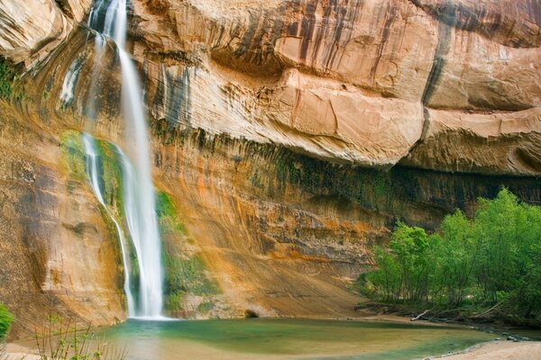 The waterfall flows from the cliff into the lake