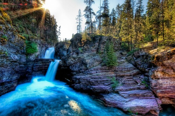 Cascada de montaña en el fondo del bosque y el sol