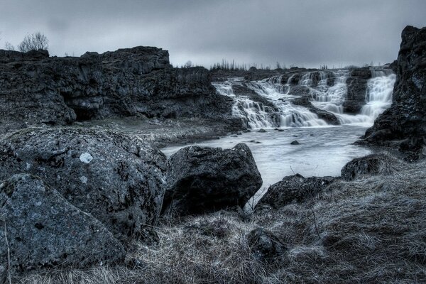 Schwarz-Weiß-Landschaft eines kleinen Wasserfalls am felsigen Flussufer