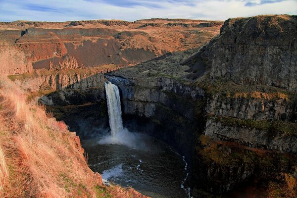 A powerful waterfall in the canyon flows into a stormy river