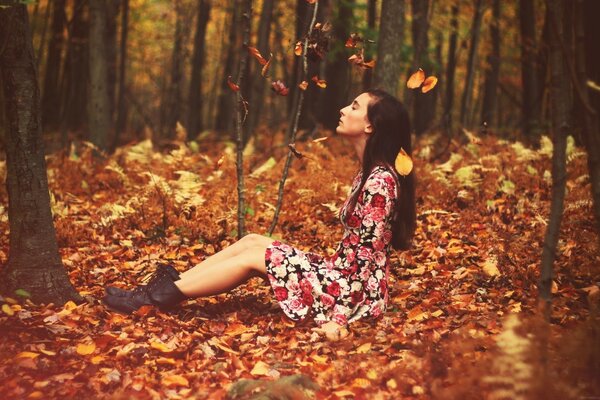 A girl in a bright dress on a carpet of orange leaves in the forest