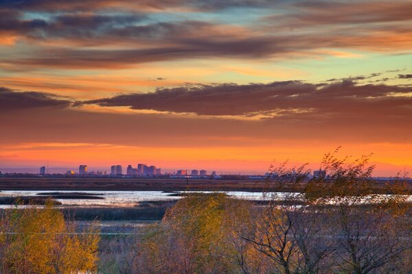 Autumn dawn with a view of a swampy lake and a city in the distance