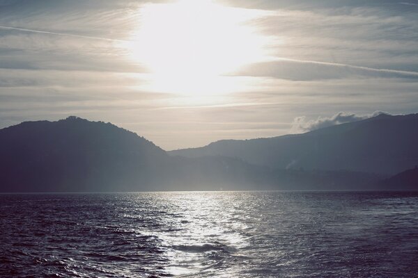 Reflection of the sun in the lake against the background of mountains