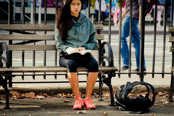 The girl is sitting on a bench near the fence