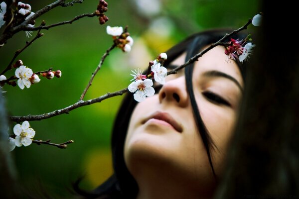 The girl inhales the fragrance of blooming flowers on a tree