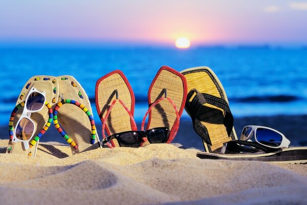 Zapatillas, gafas en la arena en el fondo de la puesta de sol del mar