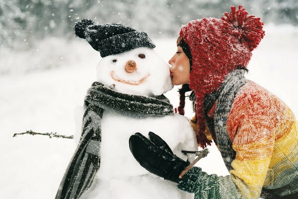 Girl kisses a snowman outdoors