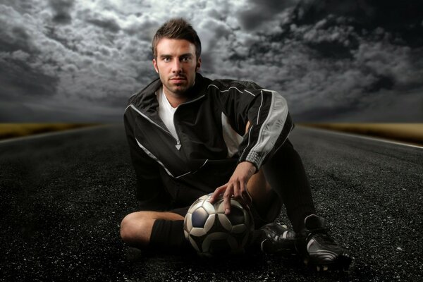 Ein Mann sitzt mit einem Ball in der Hand auf der Straße