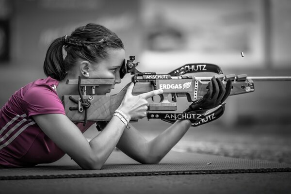 An athlete shoots a rifle in a pink T-shirt