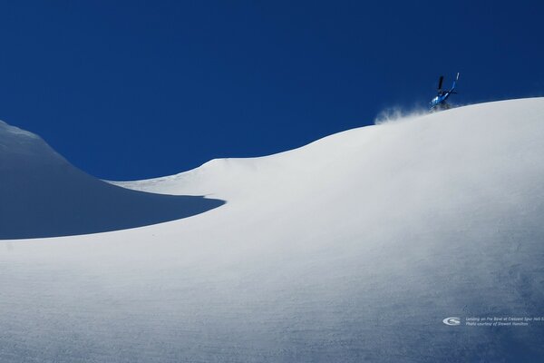 The helicopter lands on a snowy mountainside on a clear day