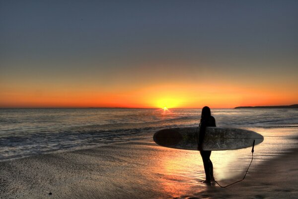 Das Surfermädchen blickt auf die Sonne, die bei Sonnenuntergang untergeht