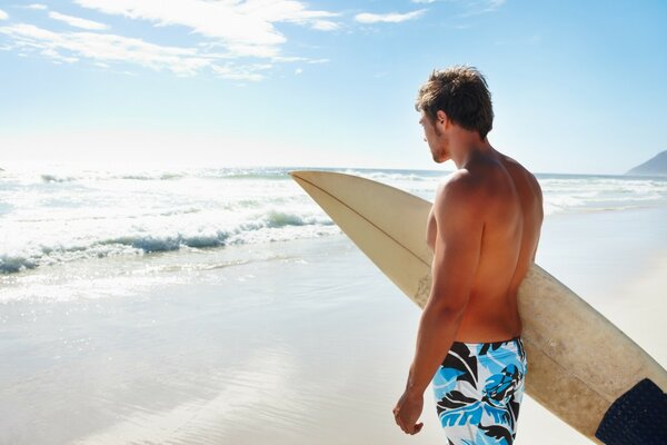 Homme avec planche de surf à la main au bord de la mer