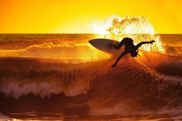 A surfer stands on a board in the ocean at sunset