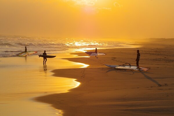 Menschen mit Surfern am Strand eines Sonnenuntergang-Sandstrandes