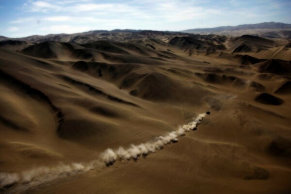 In the desert, one car drives from far away from the sand there is nothing here