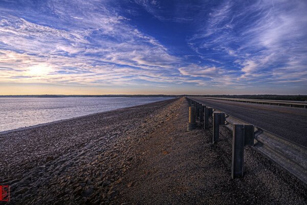 Route qui longe une plage rocheuse sur fond de coucher de soleil