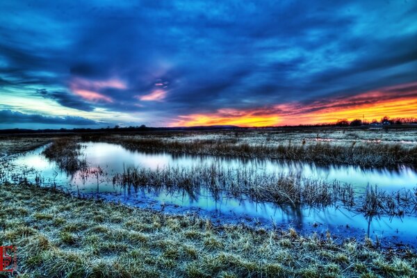 Colorful clouds on the background of grass and water