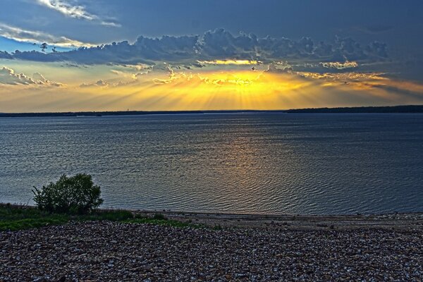 Dawn in the sky from behind the clouds by the water