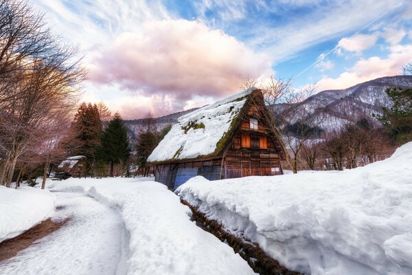 Pequeña casa cubierta de nieve en el techo al pie de la montaña y el cielo azul con nubes blancas