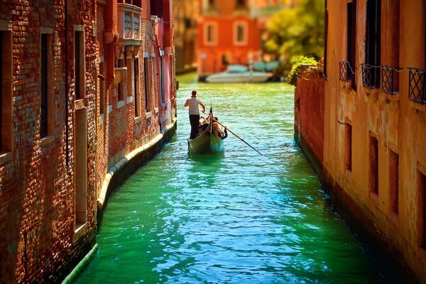 A man on a gondola floats down the street of Venice