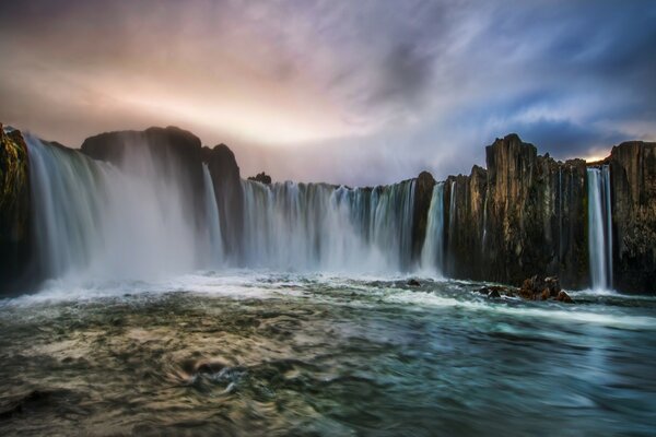 Waterfalls flow smoothly into the river below and the sky