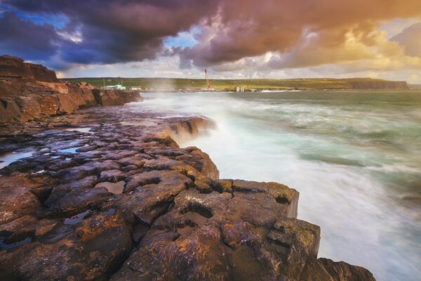 Una corriente que se precipita violentamente cayendo en cascada sobre las rocas, un faro solitario es visible en el borde de esta corriente