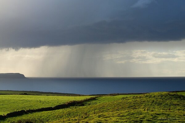 Landschaft von grünen Wiesen und Wolken , aus denen es regnet