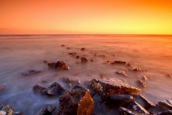 Hermosa puesta de sol en la niebla en una playa rocosa