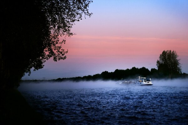 Morgennebel über dem Fluss mit Schiff