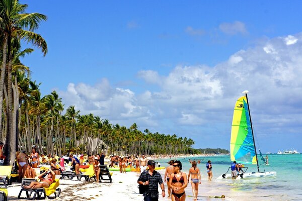 People relax on the beach under palm trees by the sea